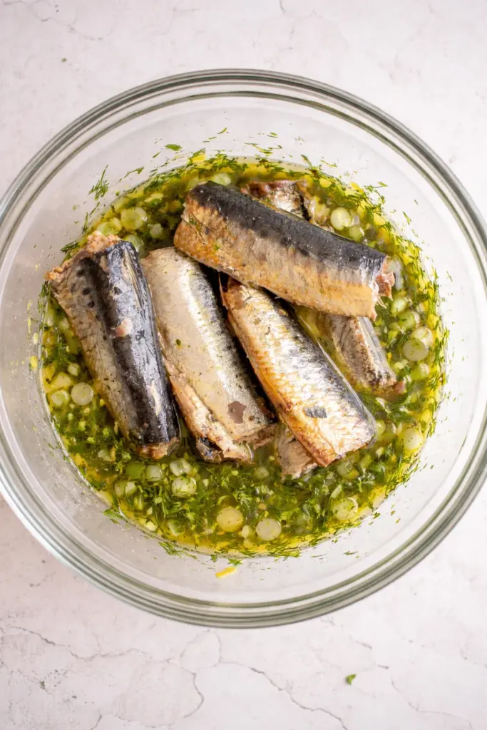 Adding canned sardine fillets to salad bowl