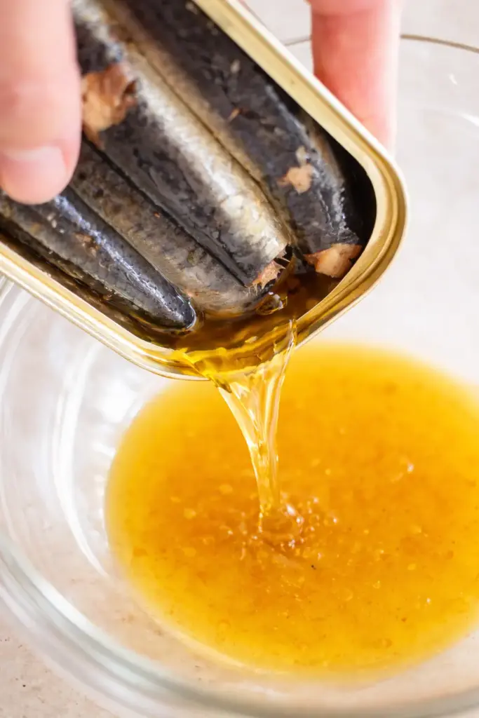 Pouring olive oil from sardine can into mixing bowl