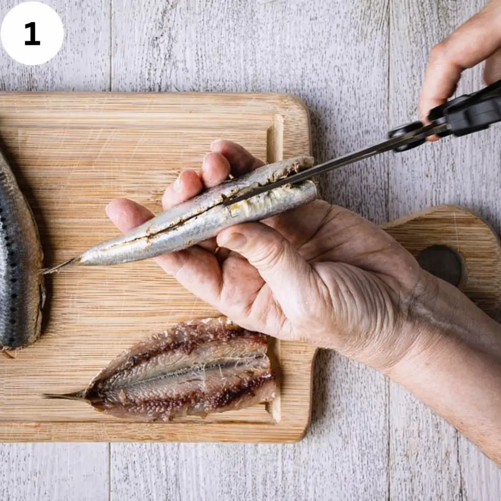Cleaning and deboning whole sardines on cutting board