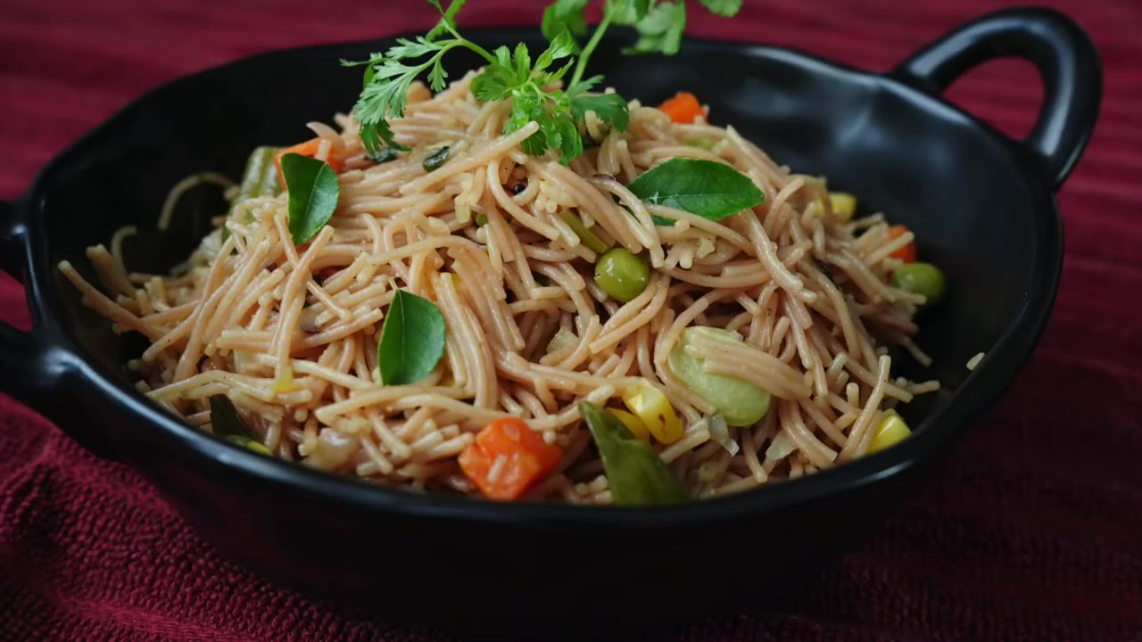 A bowl of Indian-style vegetable vermicelli upma garnished with fresh coriander and served with lemon wedges