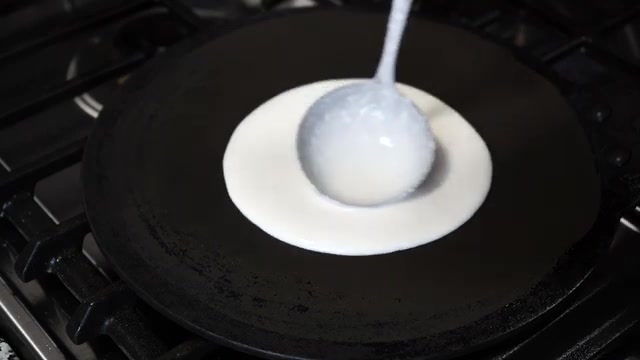 A ladleful of dosa batter poured onto the center of a hot non-stick tawa