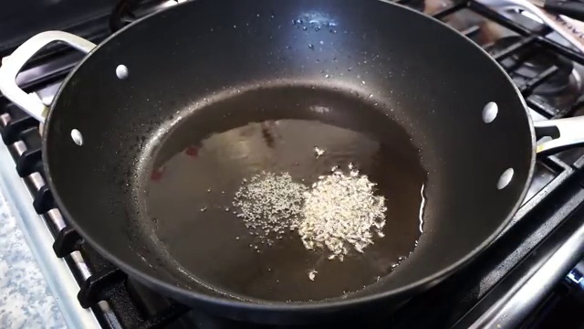 Brown mustard seeds and cumin seeds spluttering in hot oil in the pan