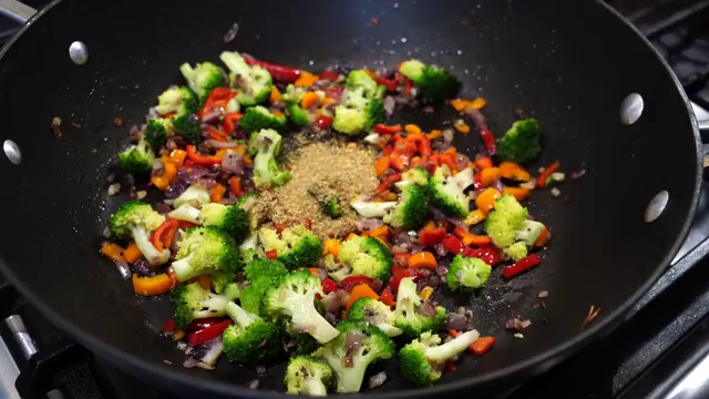 Frozen mixed vegetables including carrots, peas, and corn added to the spiced pan