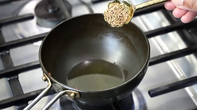 Aromatic black nigella seeds kalonji and dried red chili sizzling in hot oil in the skillet