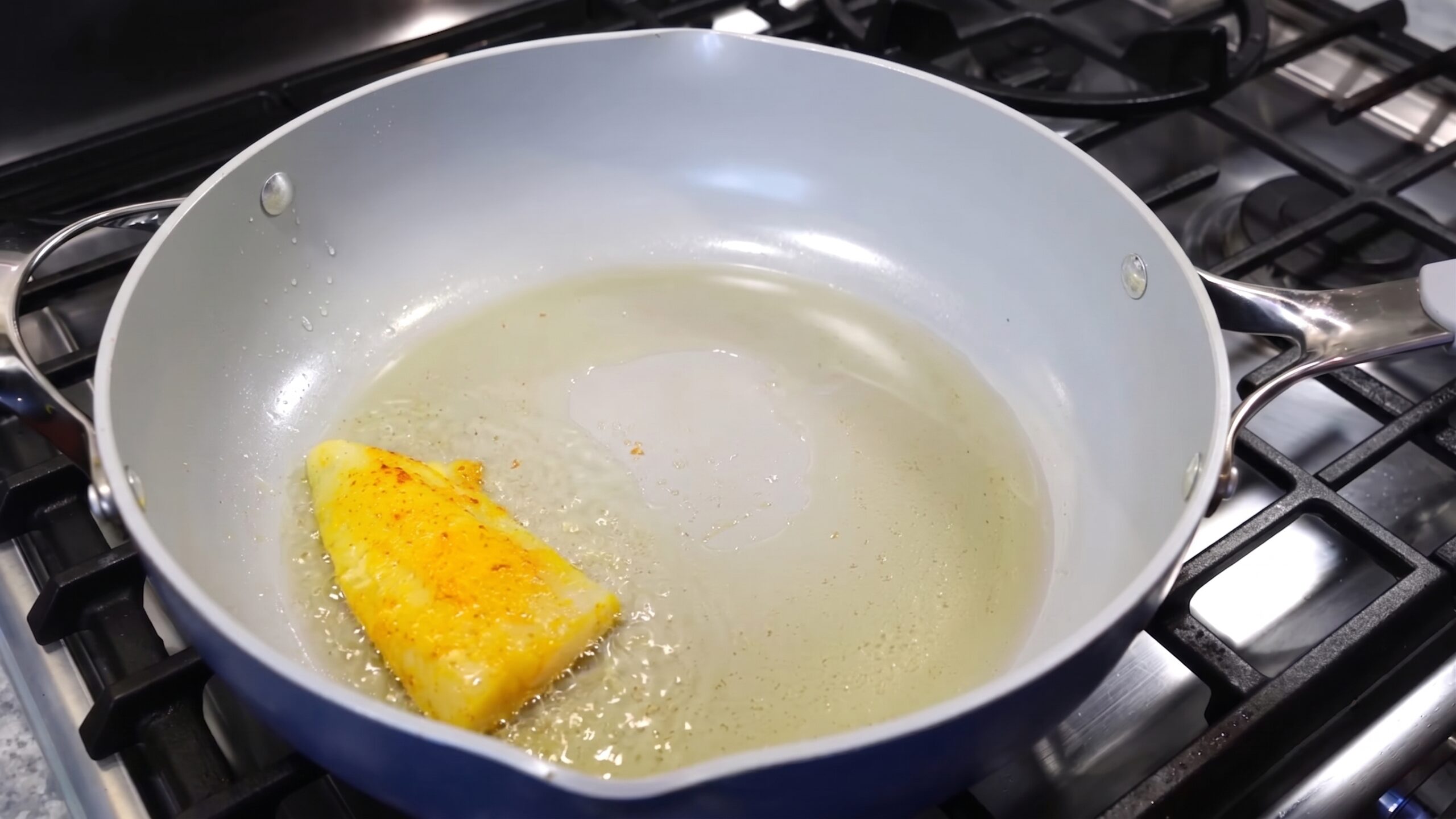 Dried bay leaf, cinnamon stick, and green cardamom pods sizzling in hot oil