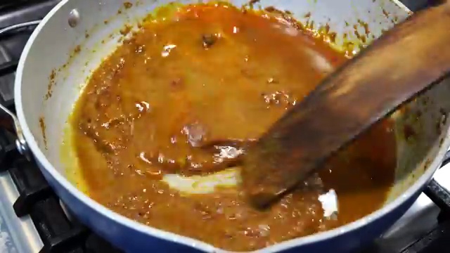 Tasting the simmering Macher Jhal gravy to adjust salt and lemon juice