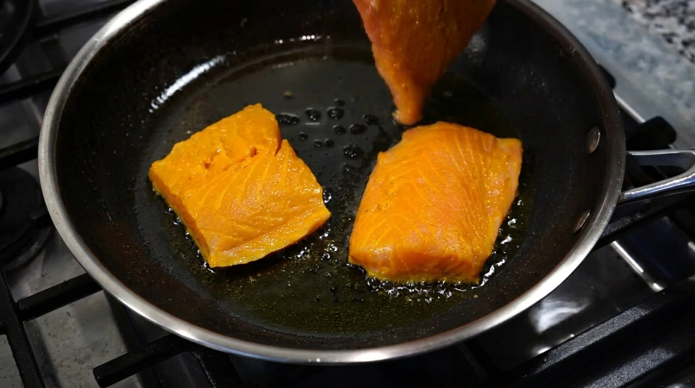 Golden spiced curry gravy spooned gently over the simmering fish fillets in the pan