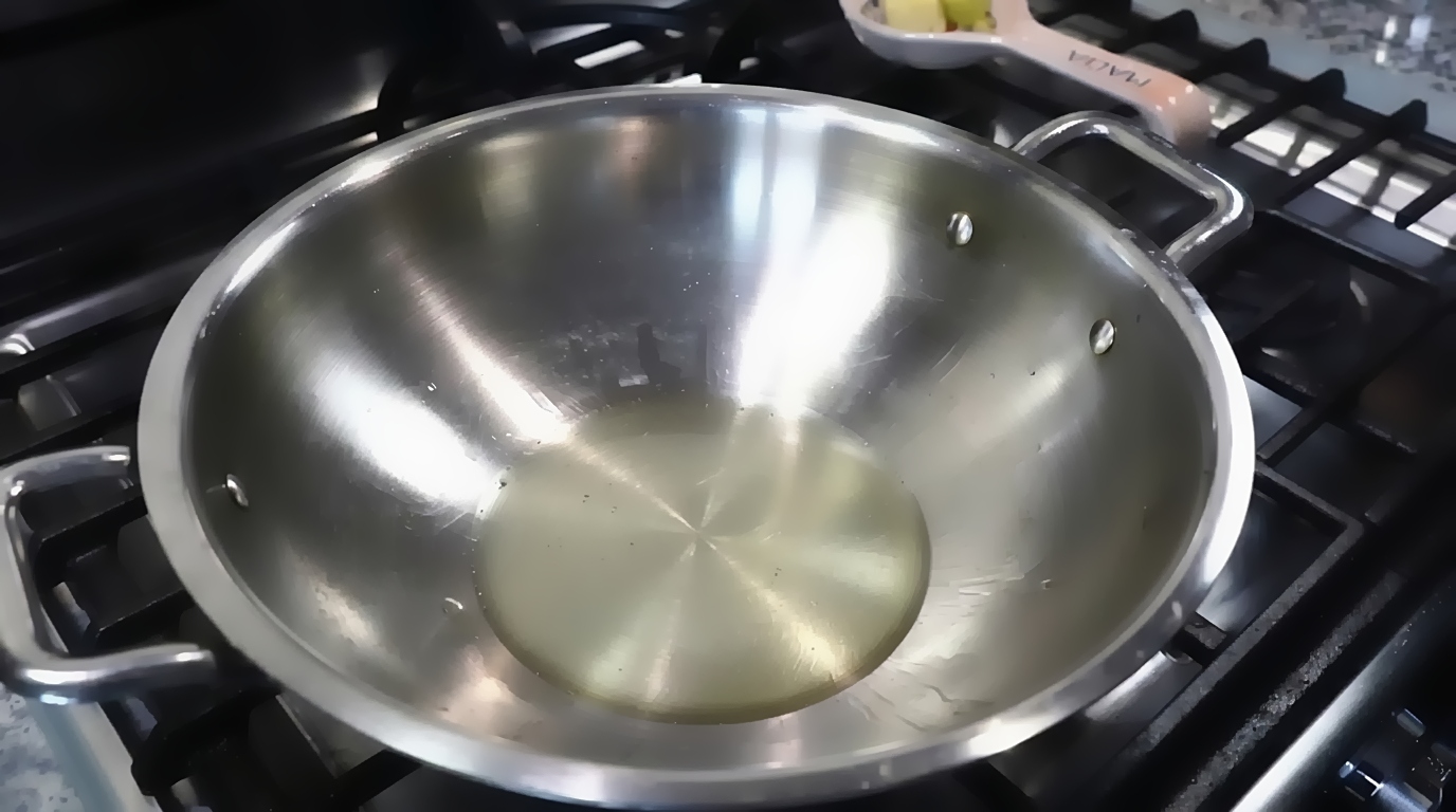Thinly sliced yellow onions added to warm cooking oil in a wide pan for black pepper chicken