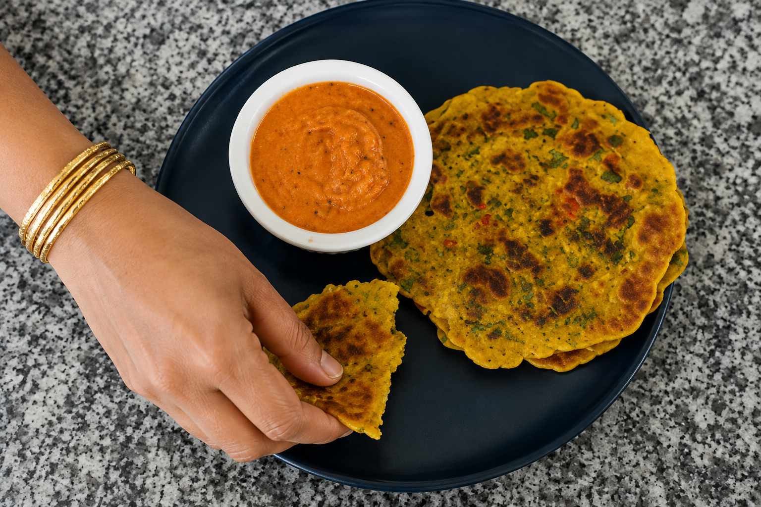 Golden vegetable besan chillas stacked on a plate with spicy red tomato sesame chutney