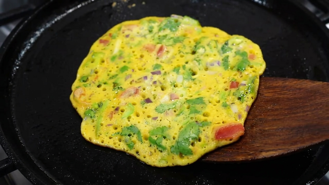 Golden besan chilla being flipped with a spatula in a frying pan