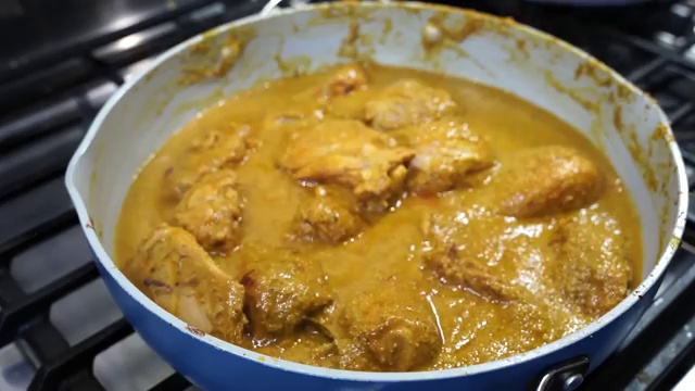 Chicken Xacuti curry simmering slowly on low heat in a covered pan until tender