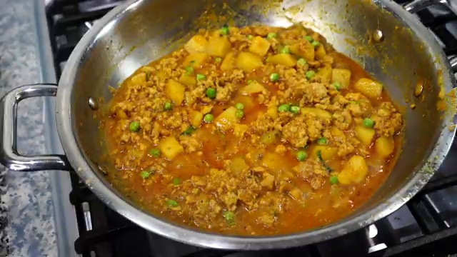 Chicken keema curry gently simmering with potatoes and green peas under a covered lid