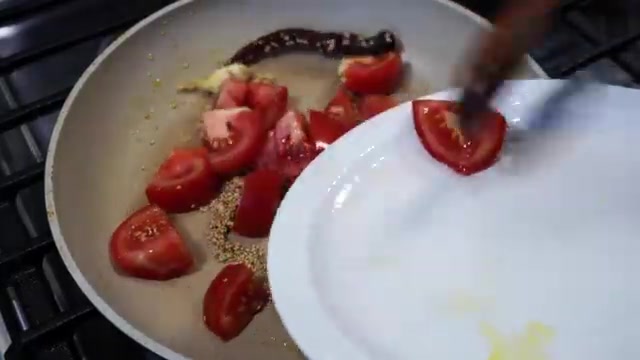 Chopped tomatoes cooking with garlic, dried chili, and sesame seeds in a pan