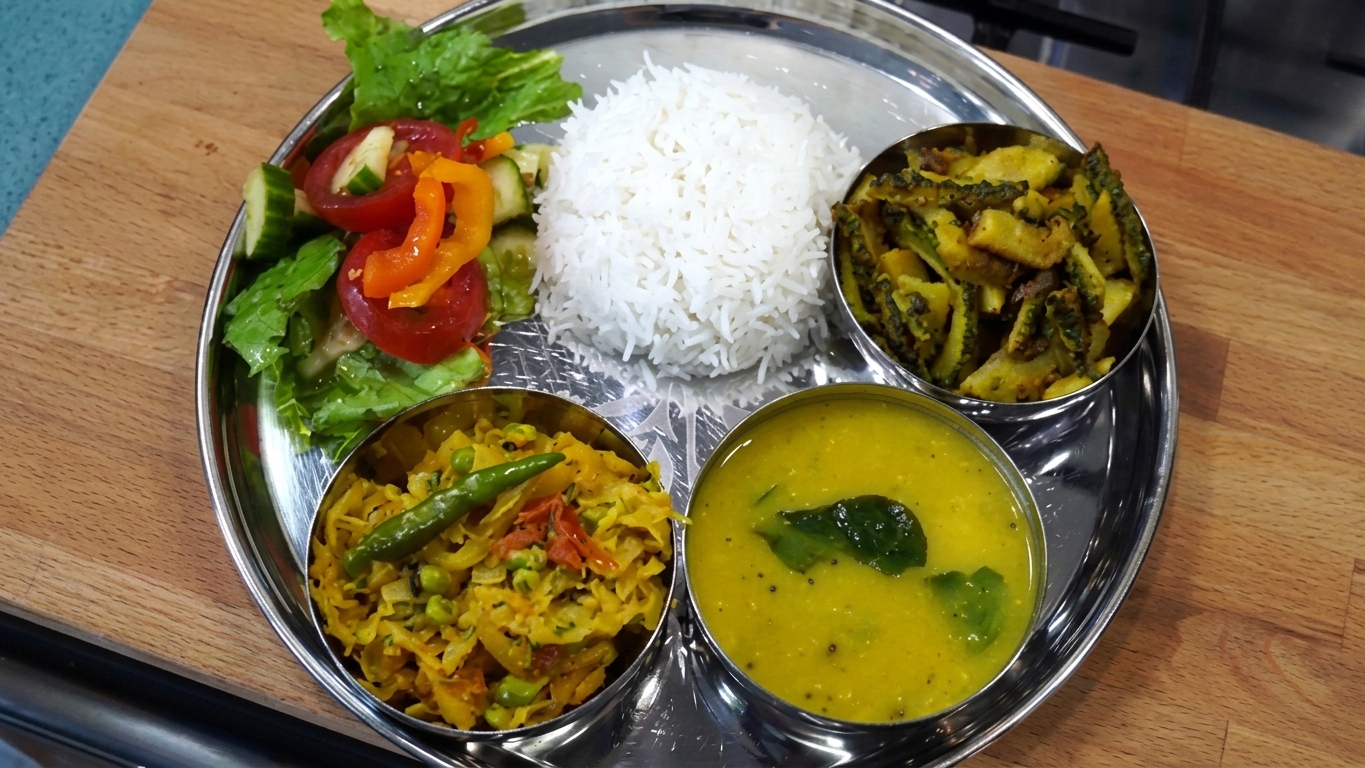 Complete Indian home-style thali meal plated with steamed rice, dal, cabbage curry, and bitter gourd potato fry