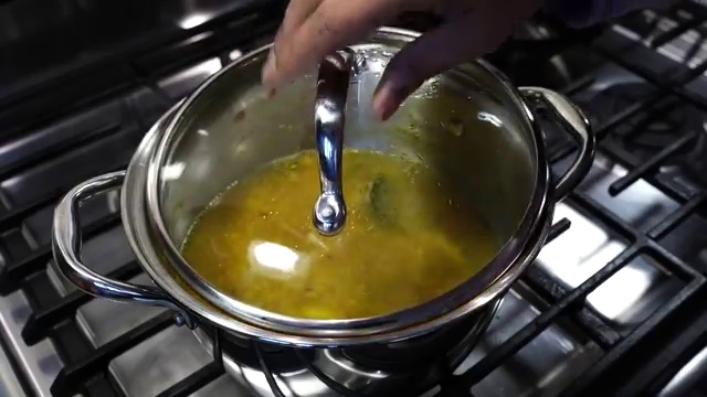 Cooked masoor dal being mashed with a traditional wooden Indian dal masher
