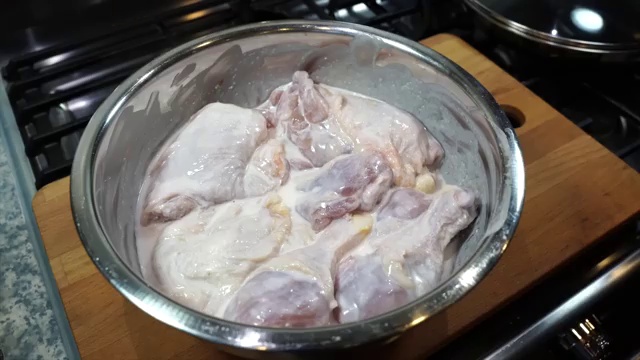 Glass bowl of buttermilk marinated chicken covered with plastic wrap ready for the refrigerator