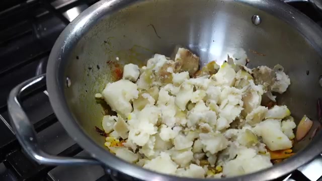 Crumbled boiled potatoes being added to the spiced onion mixture