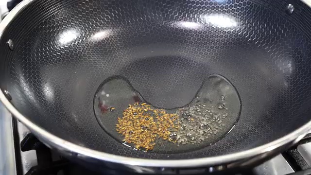 Cumin seeds and black mustard seeds sizzling and spluttering in hot cooking oil for tempering