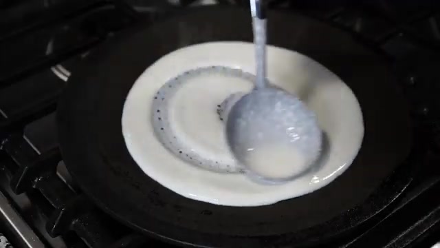 Dosa batter being gently spread outward in a circular motion across a hot tawa