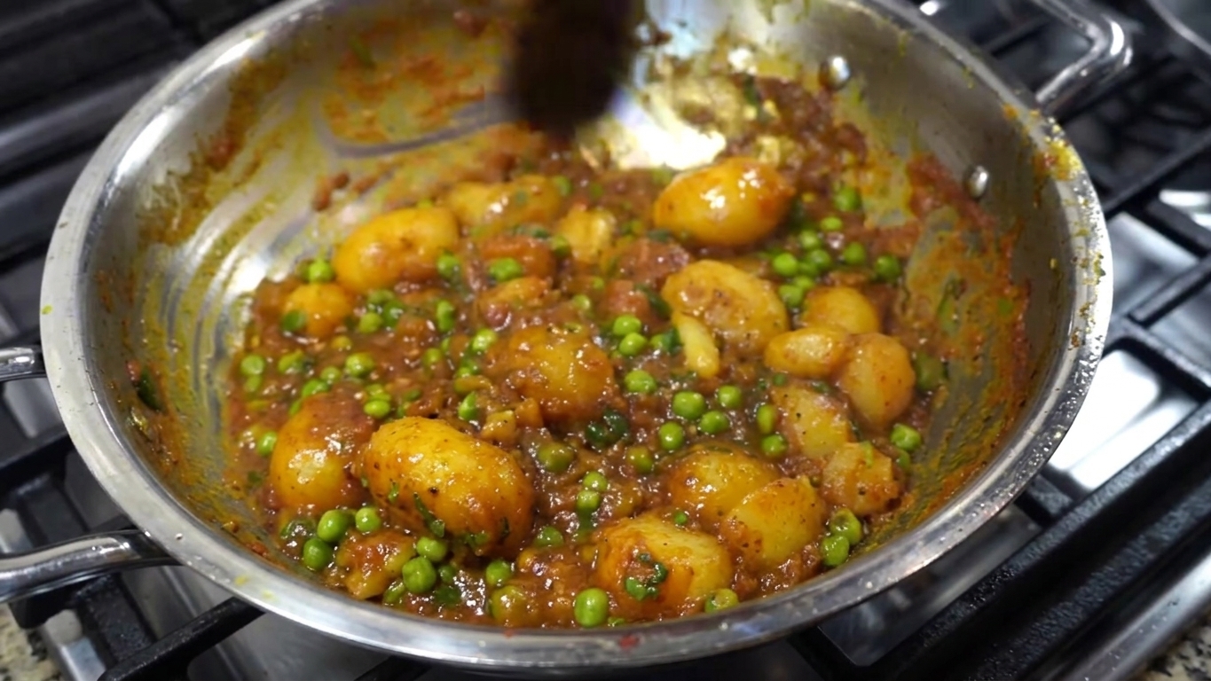Finished Aloo Dum curry with baby potatoes, green peas, tomatoes, and fresh coriander