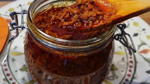 Finished vibrant red-orange green mango pickle served in a small bowl ready to enjoy