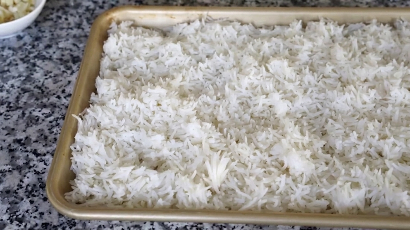 Freshly cooked white rice spread evenly on a tray to cool completely for fried rice