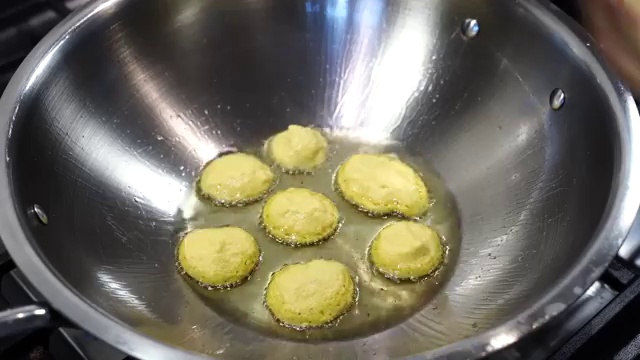 Crispy golden-brown dal bora fritters being gently flipped in the pan