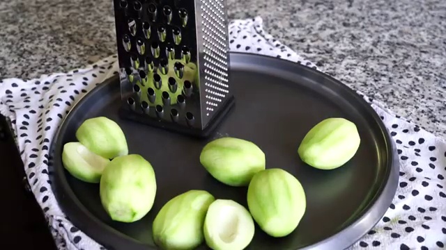 Peeled green mango being coarsely grated using the large-hole side of a box grater