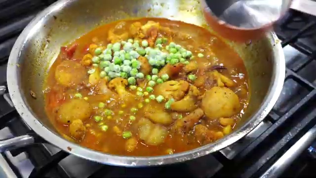 Vibrant sweet green peas added to the simmering cauliflower and potato curry