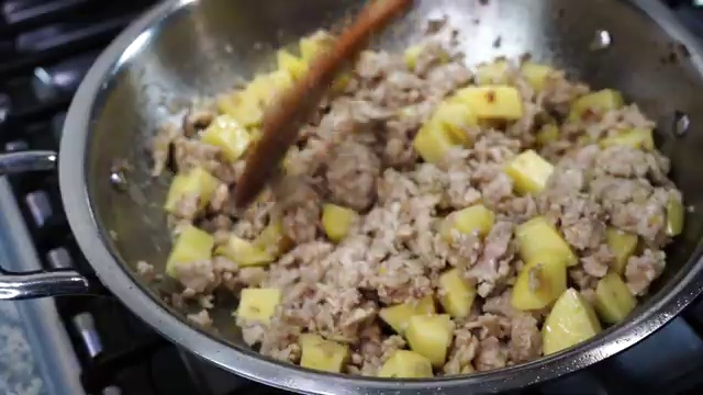 Ground chicken being broken apart with a spatula and stirred into the aromatics