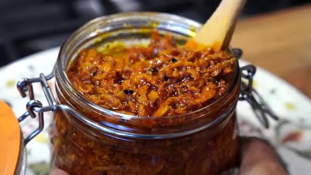 Cured green mango pickle being gently stirred with a clean, dry metal spoon