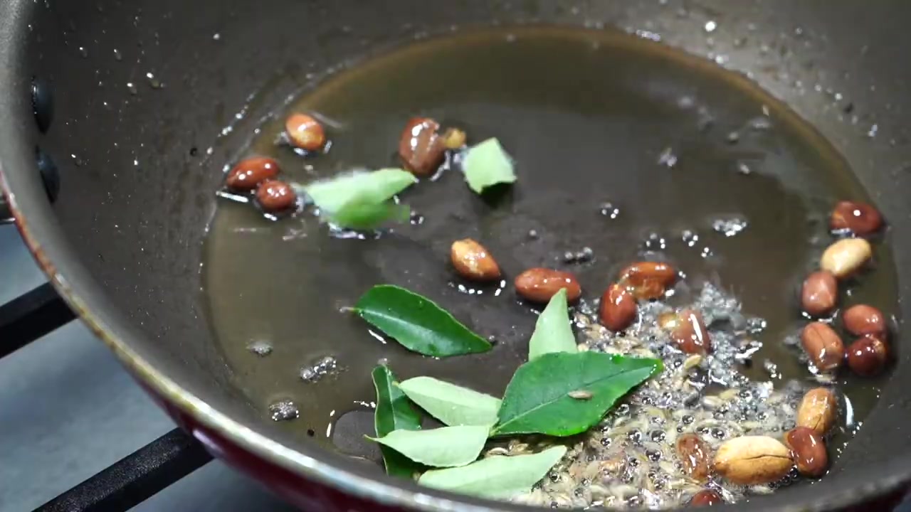 Mustard seeds, cumin seeds, peanuts, and curry leaves tempering in hot oil