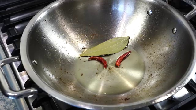 Panch phoron (Bengali five-spice) sizzling in hot oil with bay leaf and dried red chilies
