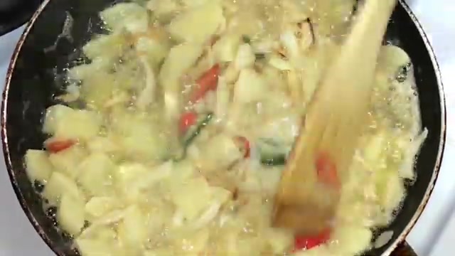 Potatoes, onions, and chilies cooking in hot oil in a non-stick pan