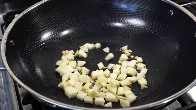 Small diced potato cubes frying in spiced oil until edges turn lightly golden