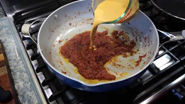 Smooth yogurt-based masala gravy being stirred constantly over low heat to prevent splitting