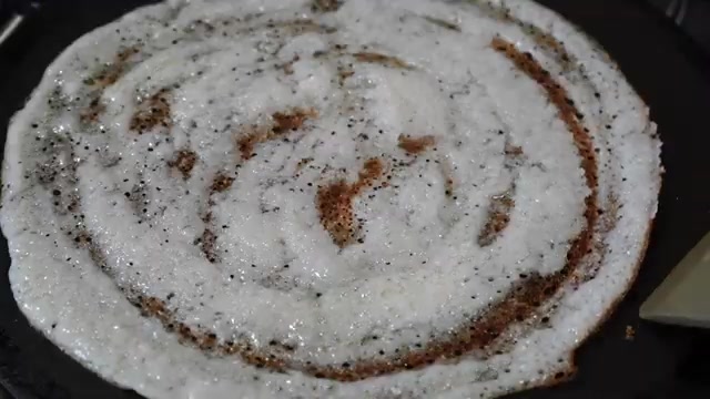 Thin dosa cooking on a tawa with golden-brown circles appearing on the surface