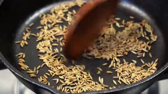Toasted cumin seeds being coarsely crushed with a mortar and pestle